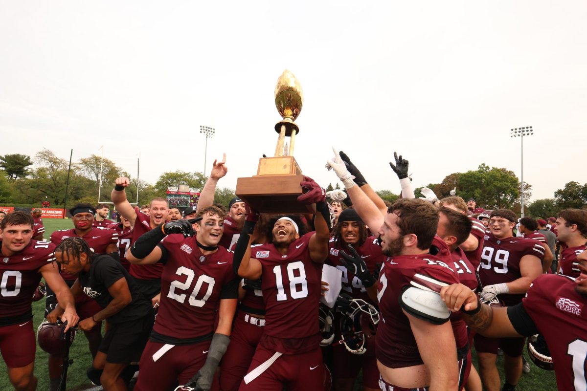 Members of the Fordham football team lift the Ram-Crusader Cup after defeating Holy Cross.