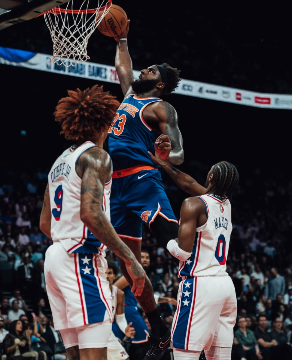 New York Knicks center Mitchell Robinson dunks over two Philadelphia 76ers defenders.